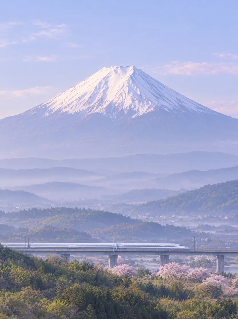 Illustration of a white bullet train crossing a viaduct below Mount Fuji.
